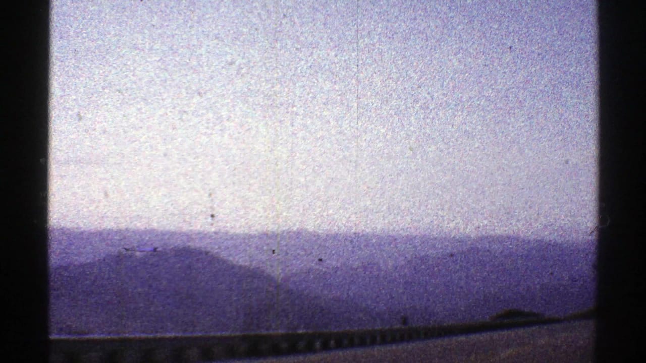 Hazy mountain ridges beneath a pale sky with a roadside guardrail along the bottom edge.