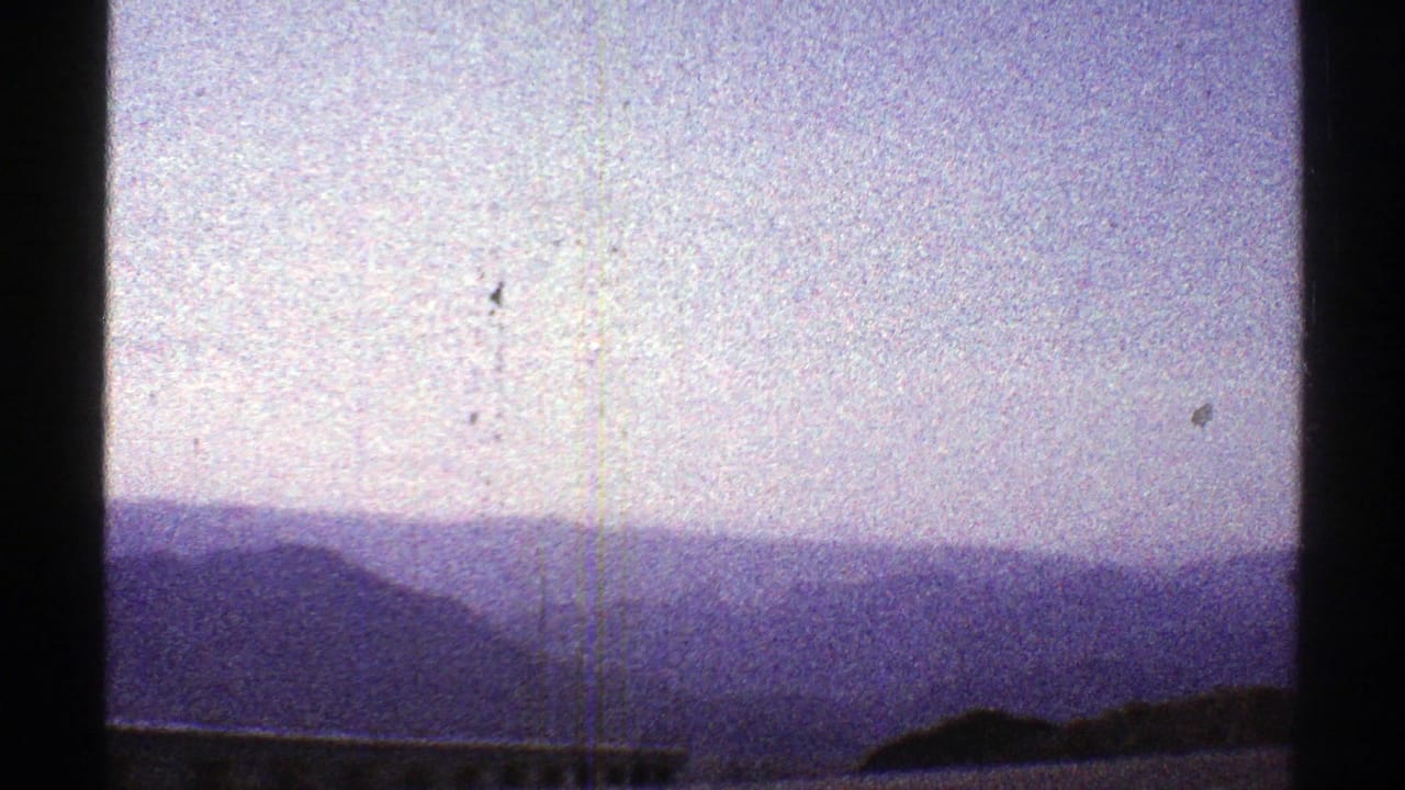 1969 Arizona 8mm frame showing distant hazy mountains under a pale blue-purple sky with visible film grain and gate edges.