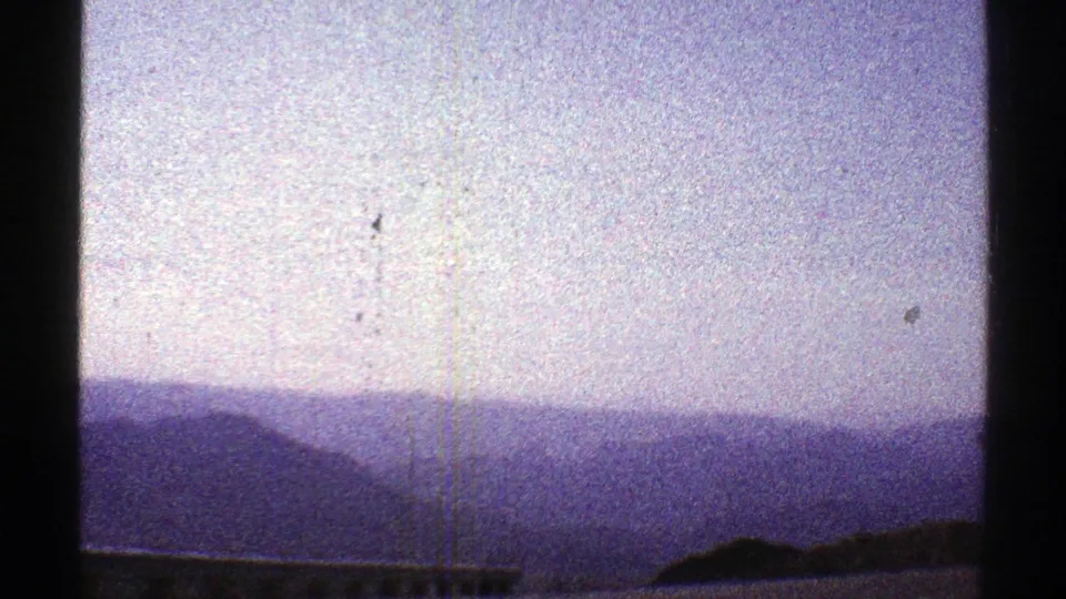 1969 Arizona 8mm frame showing distant hazy mountains under a pale blue-purple sky with visible film grain and gate edges.