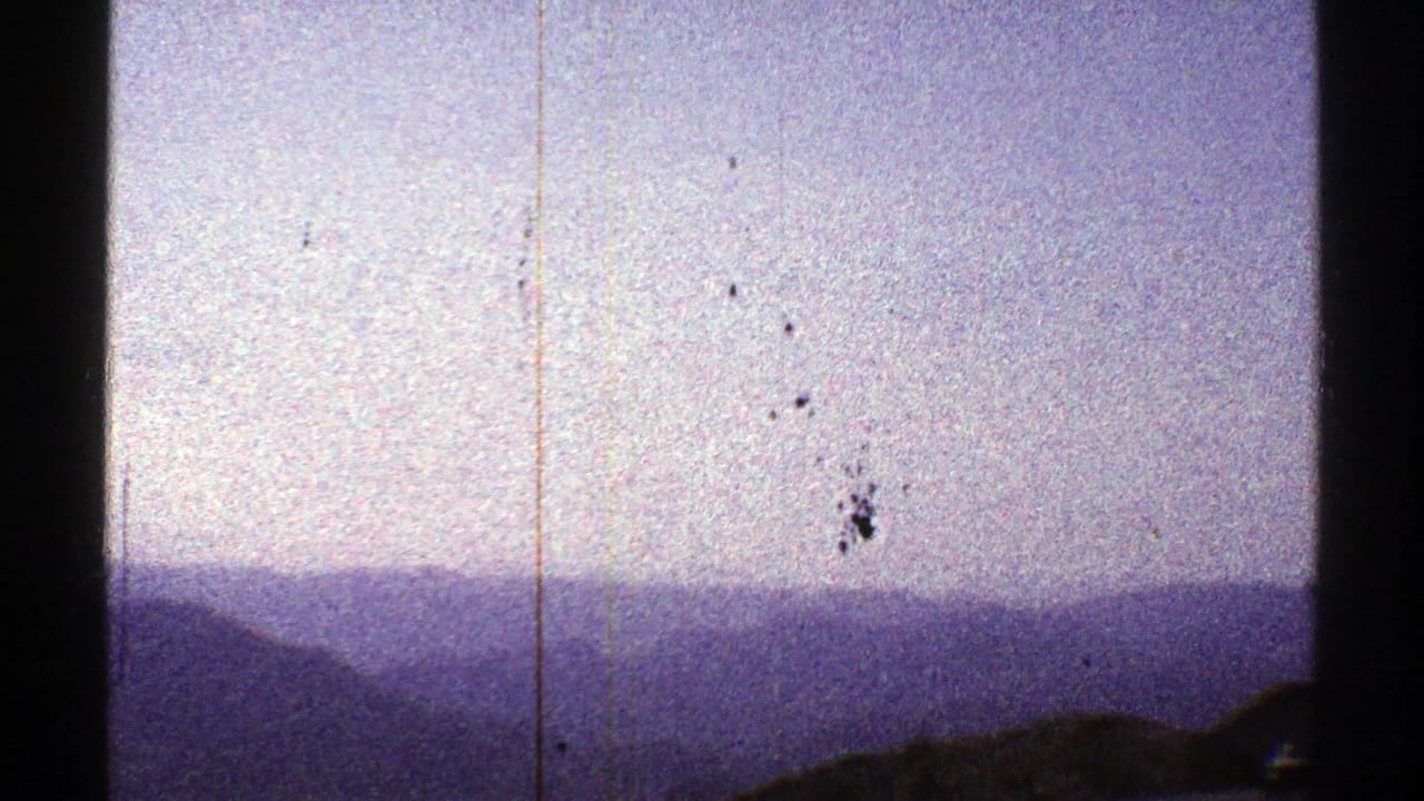 Pale sky and distant blue mountain ridges with a small dark bird above the horizon.