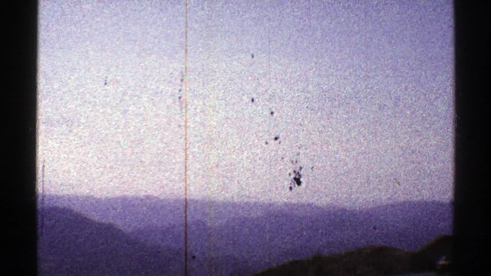 1969 Arizona landscape frame with a small bird crossing a pale, grainy sky above distant blue mountain ridges.