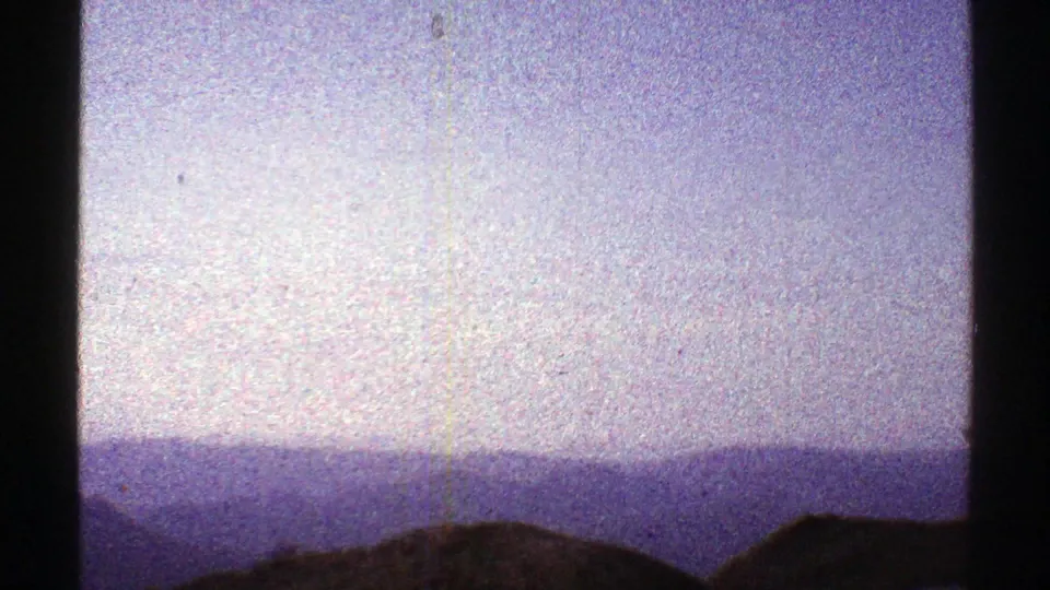 1969 Arizona 8mm frame showing a dark foreground ridge and layered hazy mountains beneath a faded pale sky.