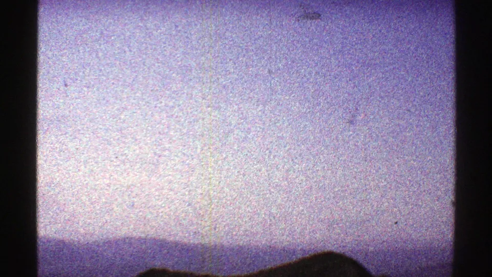 Faded 1969 Arizona 8mm frame with pale sky, distant blue ridges, and a dark low hill in the foreground.