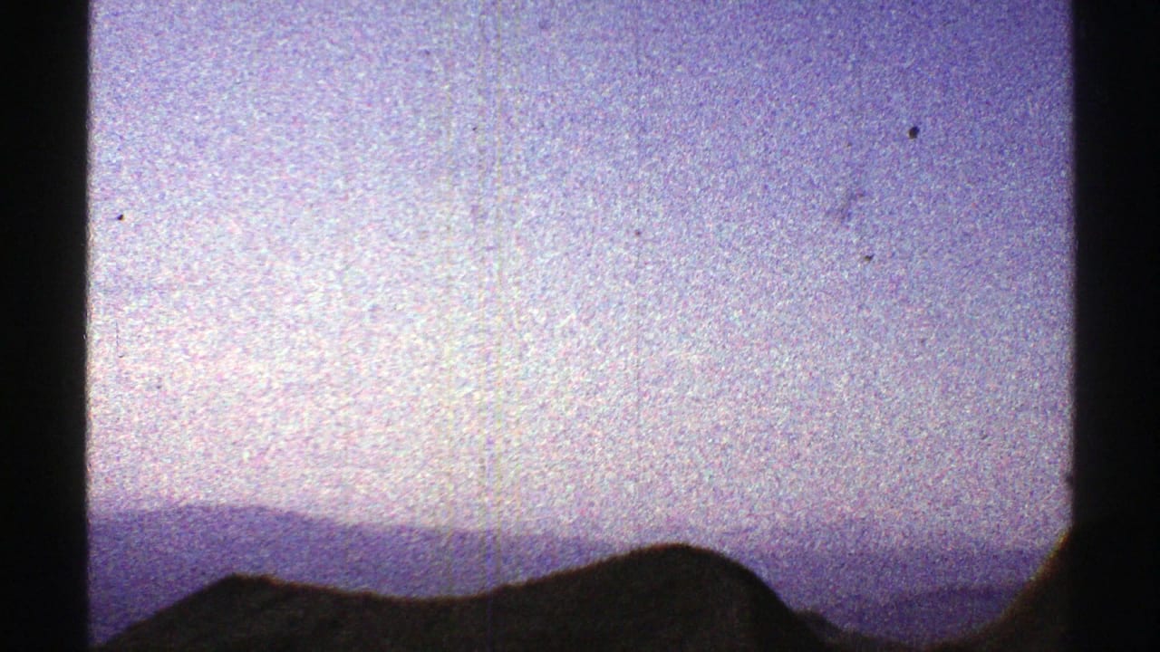 1969 Arizona 8mm frame showing a dark mountain ridge and layered distant hills under a hazy blue sky.