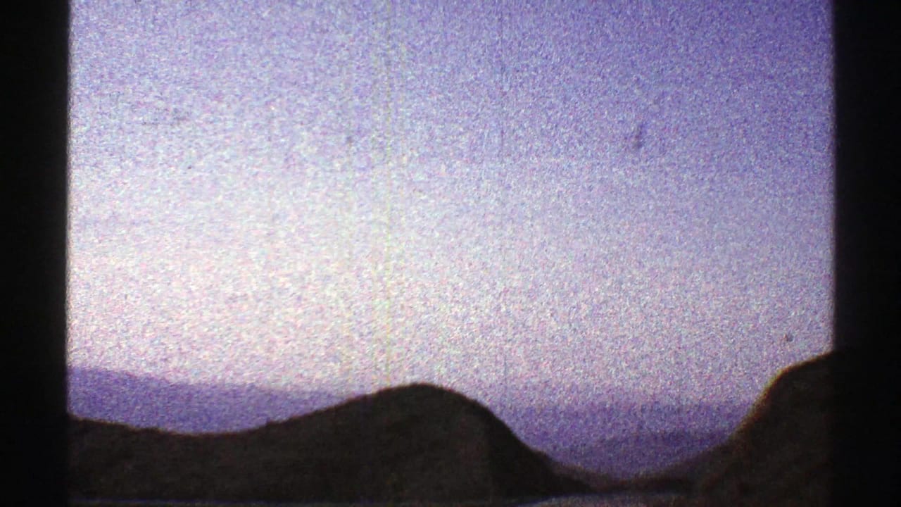 1969 Arizona 8mm travel frame with layered desert hills and a rounded mountain silhouette below a pale sky.
