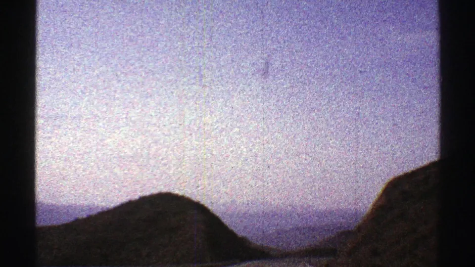 1969 Arizona home-movie frame showing a dark foreground hillside with hazy mountains and open sky beyond.