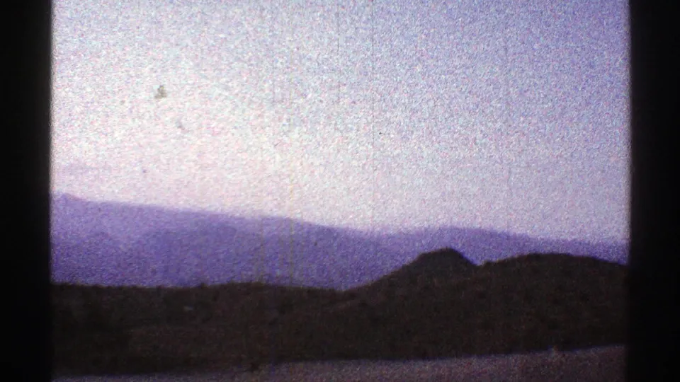 1969 Arizona 8mm frame with a broad mountain range, shadowed foreground, and hazy blue sky.