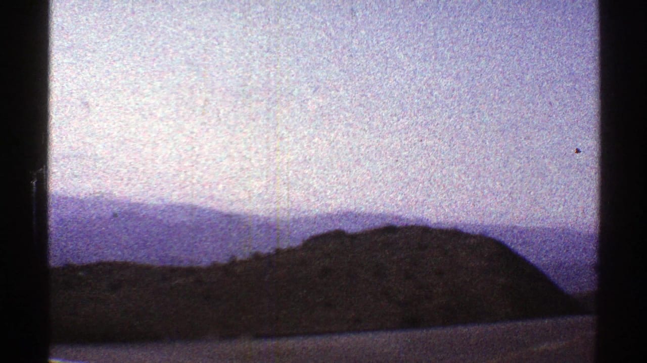Hazy ridges seen through dark vertical window bars on grainy 8mm film.
