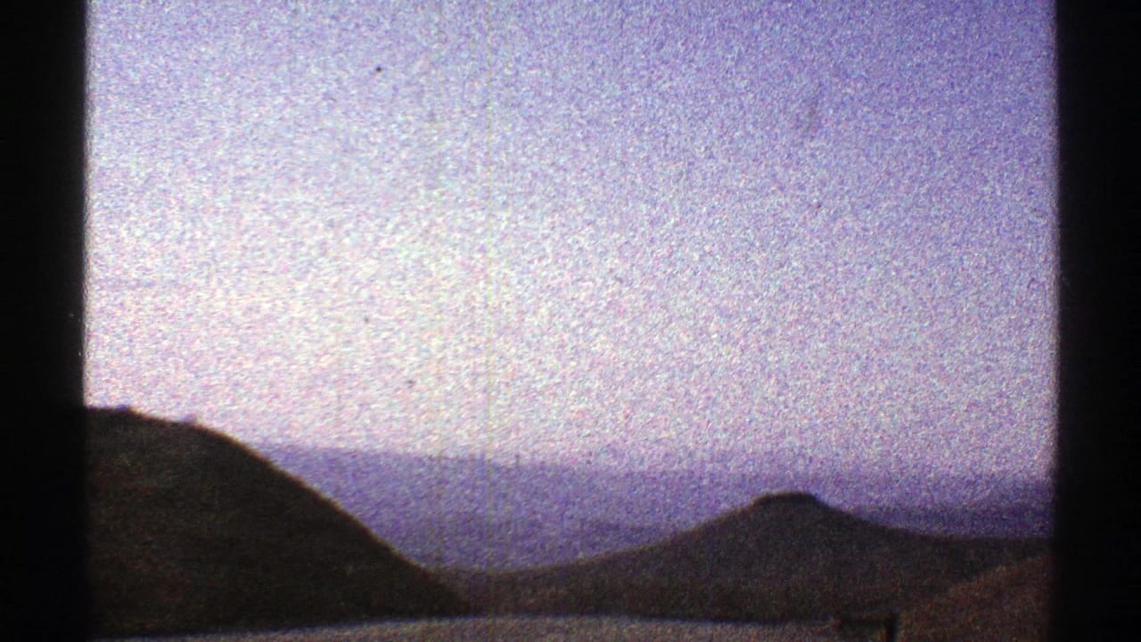 Dark hills and distant mountains under a pale grainy sky, framed by vertical bars.