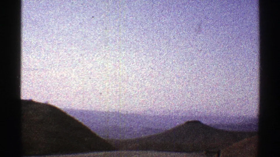1969 Arizona travel frame with silhouetted hills, distant mountain layers, and a pale overcast sky behind window bars.