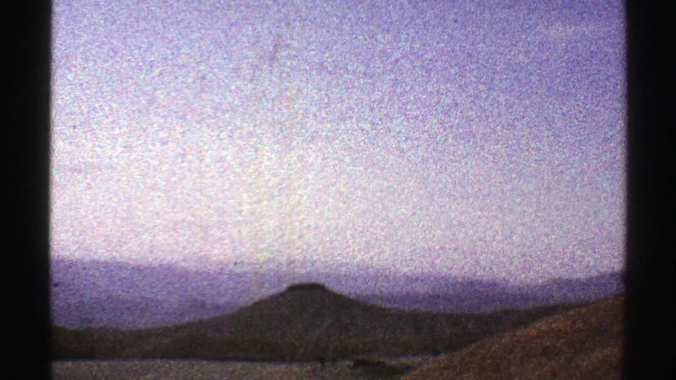 1969 Arizona 8mm frame showing a low mountain ridge, hazy blue-purple sky, and dark foreground from a moving viewpoint.