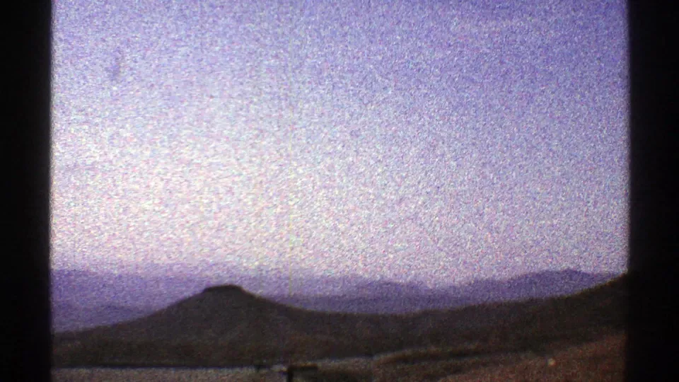 1969 Arizona home-movie frame with distant ridgelines, a low hill, pale sky, and dark vehicle or window framing.