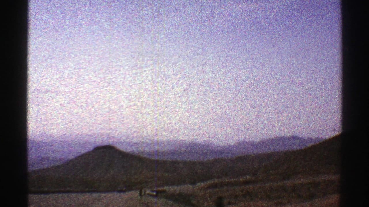 Desert hills and distant mountains under a pale sky, seen through dark film-frame edges.
