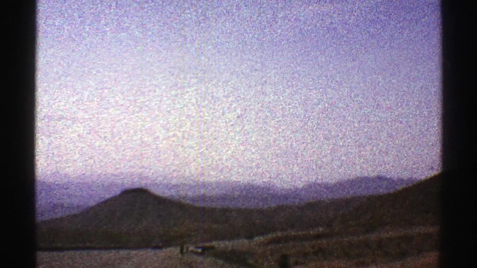 1969 Arizona 8mm frame showing arid hills and distant low mountains from a moving travel viewpoint.
