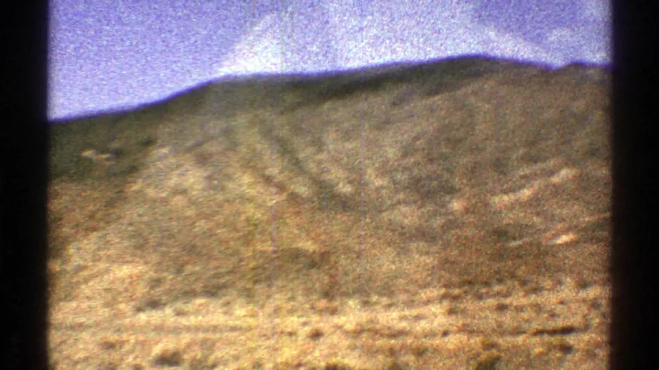 1969 Arizona 8mm frame with sloping desert terrain, low hills, and visible dark film-frame borders.