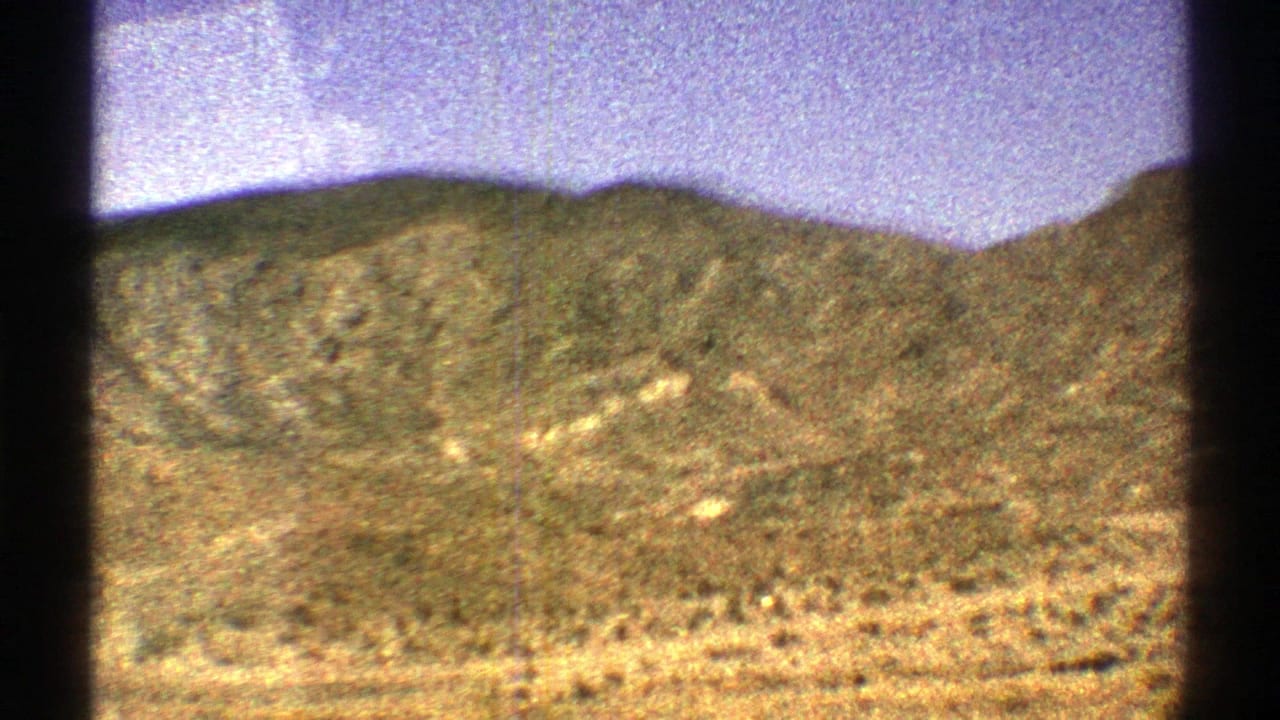 Desert hills with sparse shrubs beneath a purple sky, framed by dark film edges.