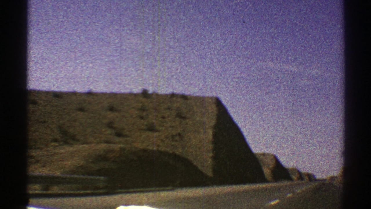 1969 Arizona road-view frame with a large rocky embankment, hazy sky, and dark window framing from the vehicle.