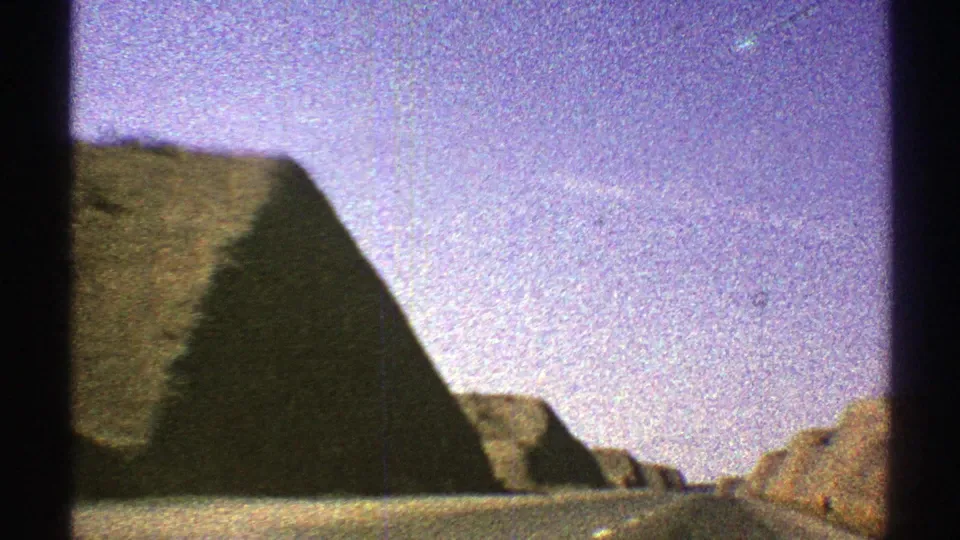 1969 Arizona 8mm frame looking forward along a desert roadway between rocky slopes from a moving vehicle.