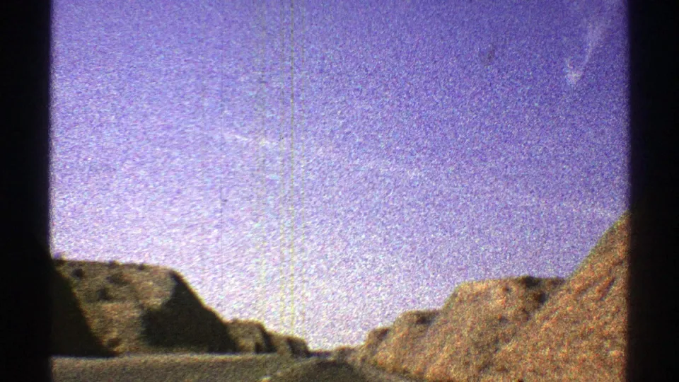 1969 Arizona travel frame showing rocky desert hills beside a road, with visible 8mm grain and window framing.