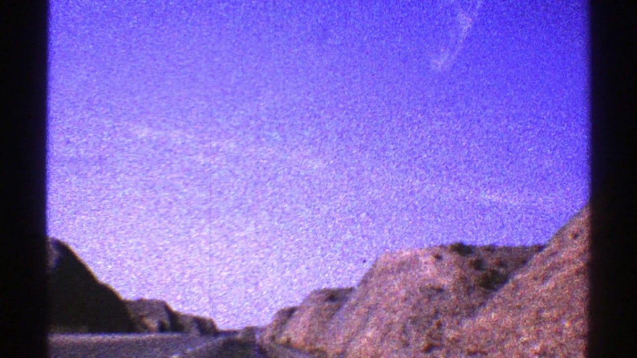 1969 Arizona 8mm frame showing a grainy purple-blue sky over brown desert rock formations near a canyon.