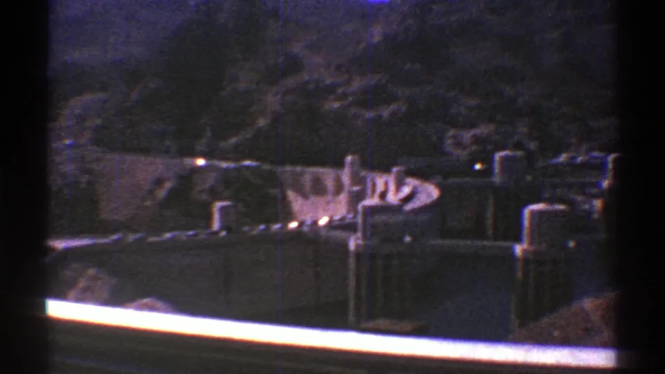 1969 Arizona home-movie frame showing a wide view of dam towers and concrete walls against a dark canyon backdrop.