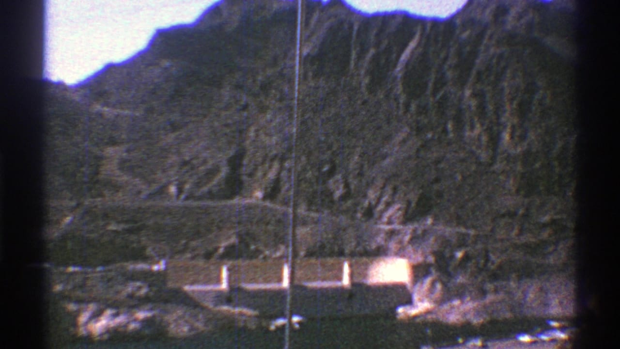 Distant Hoover Dam structures below rugged canyon walls with dark 8mm frame edges.