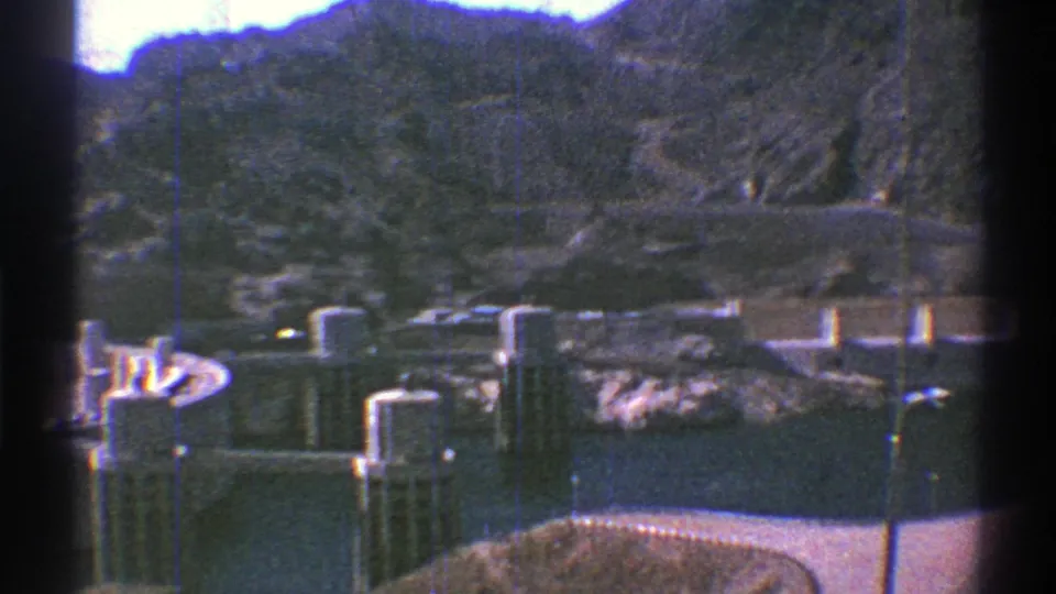 1969 8mm frame of Hoover Dam showing the dam face, intake or spillway towers, buildings, water, and surrounding canyon.