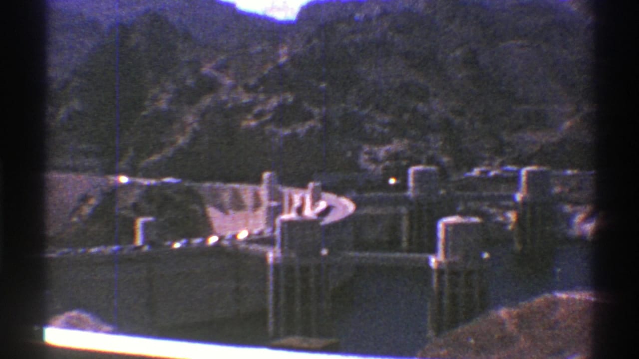 1969 Arizona 8mm view of a concrete dam set below rocky mountains, seen through dark gate edges.