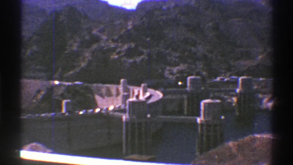 1969 Arizona 8mm view of a concrete dam set below rocky mountains, seen through dark gate edges.