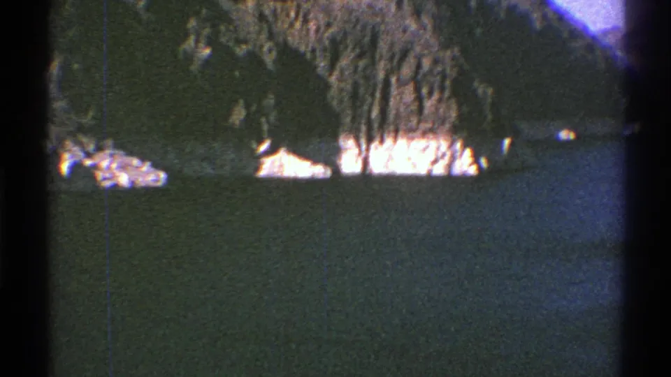 1969 Arizona 8mm view of reservoir water, rocky shore, and steep mountain slope with strong sunlight.