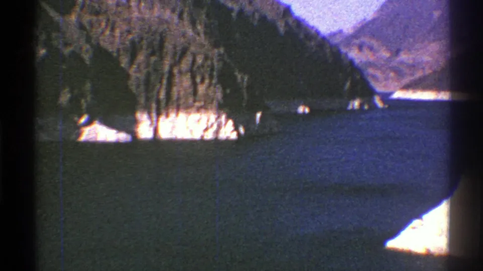 1969 Arizona 8mm frame of blue reservoir water, a rocky shoreline, and distant mountain terrain.