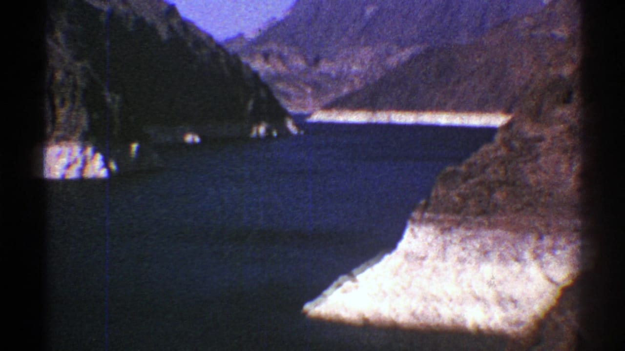 1969 Arizona home-movie frame with a wide blue waterway, light cliff edges, and distant rugged mountains.