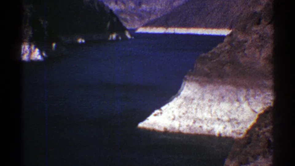 1969 Arizona 8mm frame showing a pale triangular cliff face projecting above dark blue canyon water.