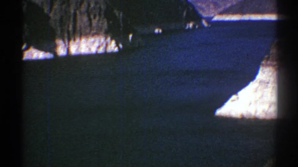1969 Arizona home-movie frame of blue canyon water, white cliff bands, dark slopes, and mountains in the distance.