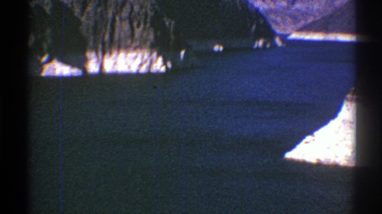 1969 Arizona 8mm frame showing blue lake water, pale shoreline, and grey desert mountains through soft, faded film color.
