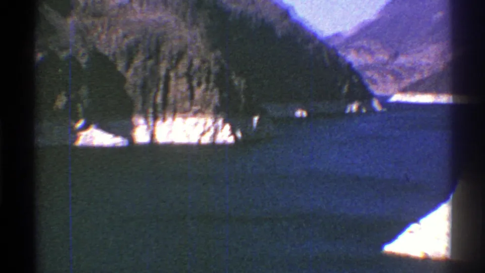 Arizona home-movie frame from 1969 showing blue water, bright shoreline, and grey mountains with visible 8mm grain.