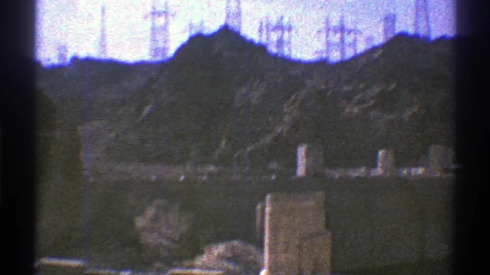 1969 Arizona 8mm frame showing utility structures and transmission towers set against grey mountains and bright sky.