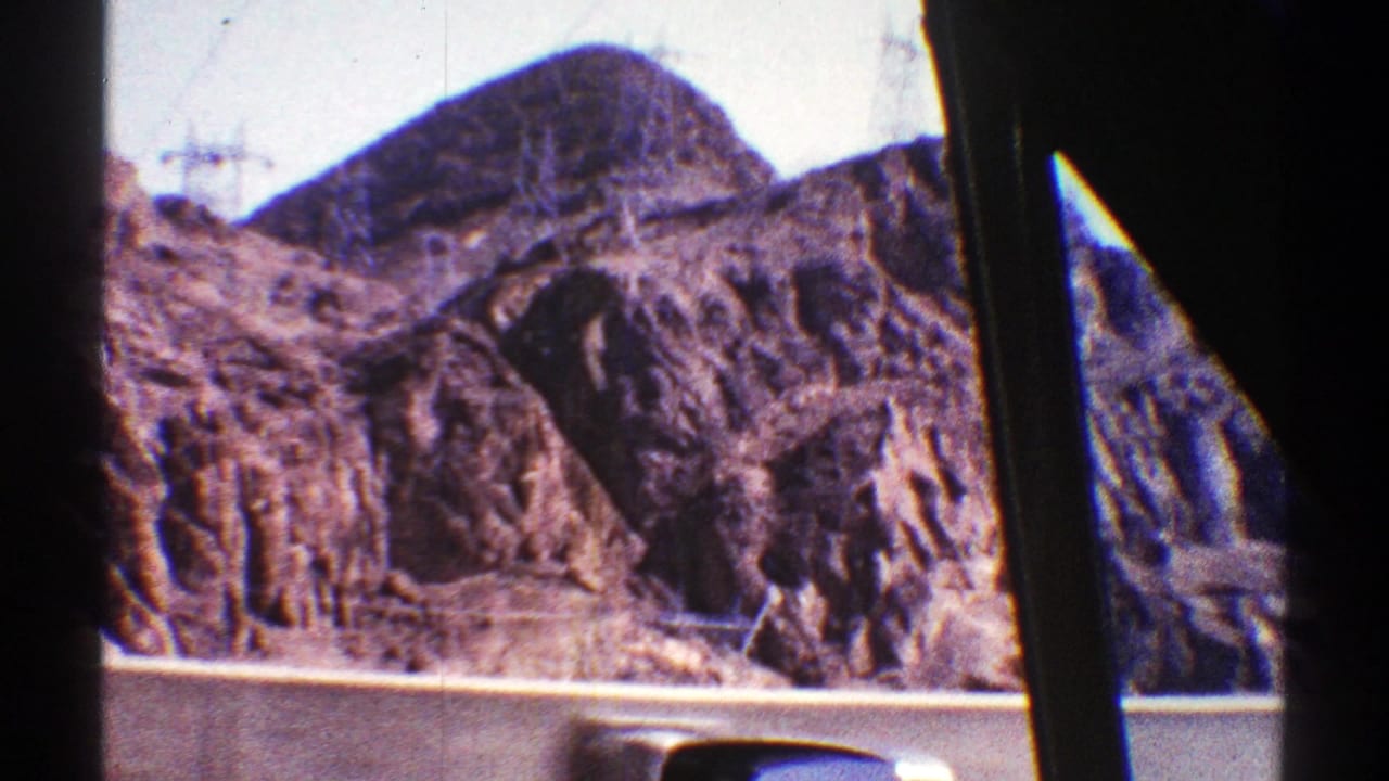 1969 Arizona desert roadway view with rugged mountains, utility towers, and dark car-window pillars crossing the frame.