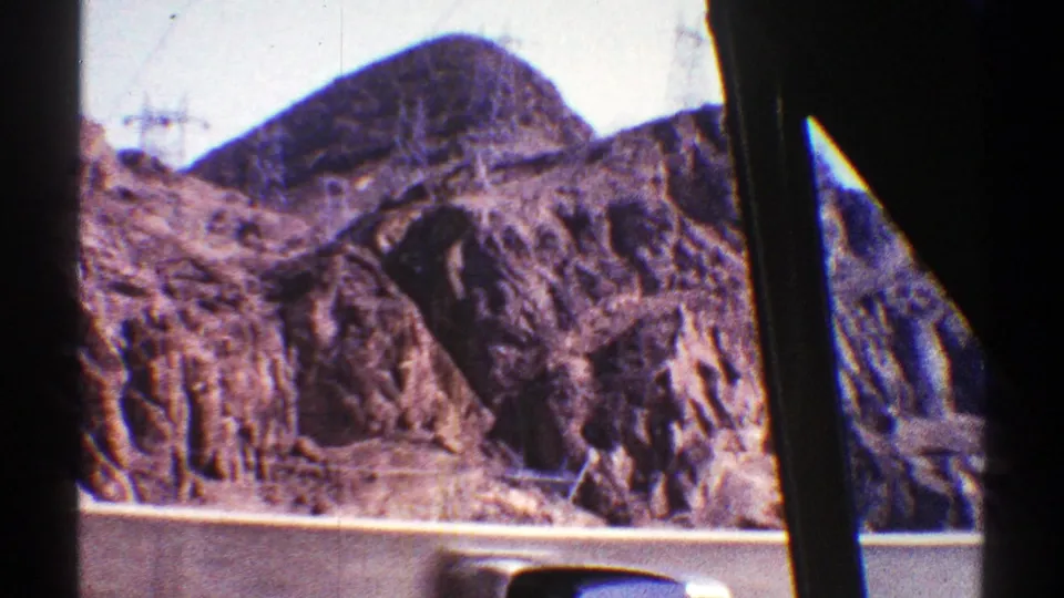 1969 Arizona desert roadway view with rugged mountains, utility towers, and dark car-window pillars crossing the frame.