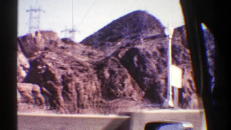 Car-window view of Arizona desert mountains in 1969, with power-line structures and a highway barrier along the road.