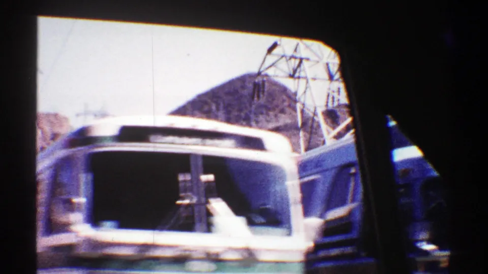 1969 Arizona highway view from inside a car, showing a bus in the adjacent lane, another vehicle edge, power lines, and desert hills.