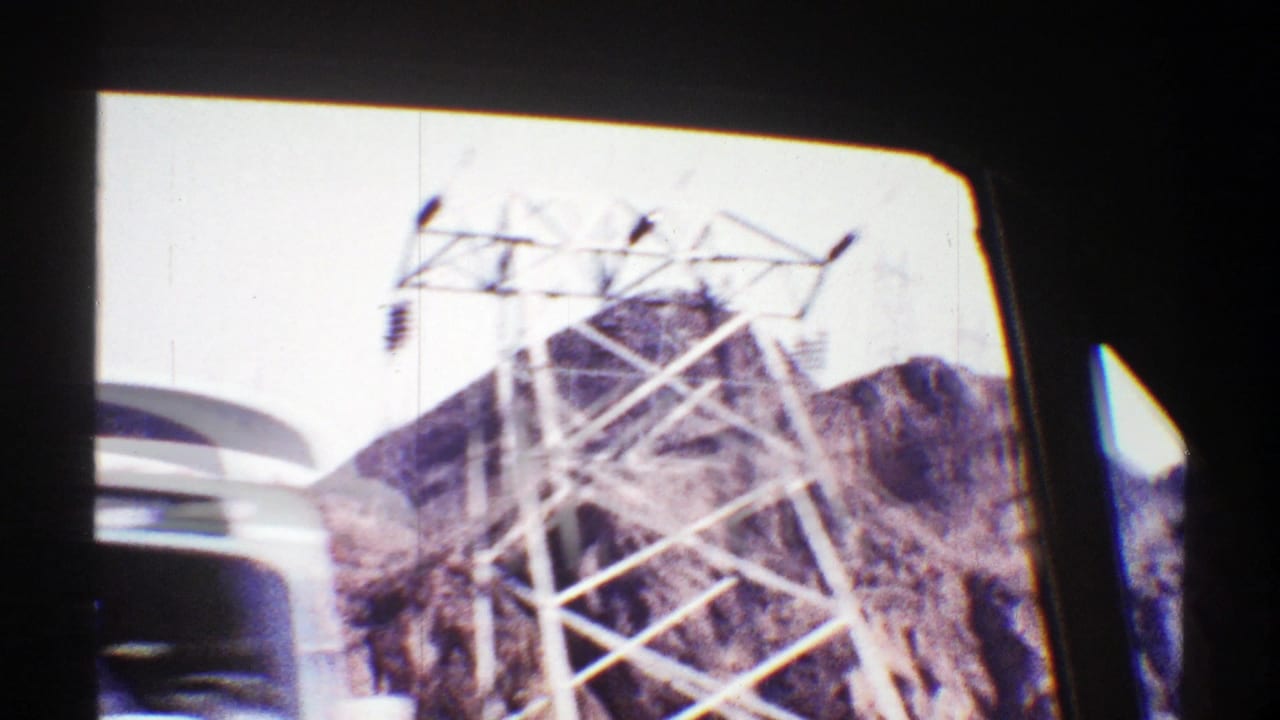 Steel electrical tower and rocky desert hill seen through a dark window frame.