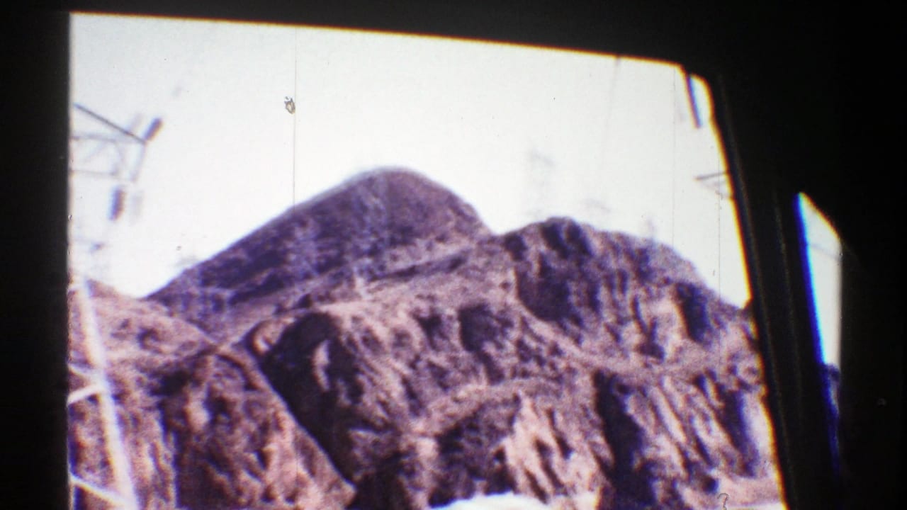 Rocky desert mountain and partial electrical tower framed by dark window posts.