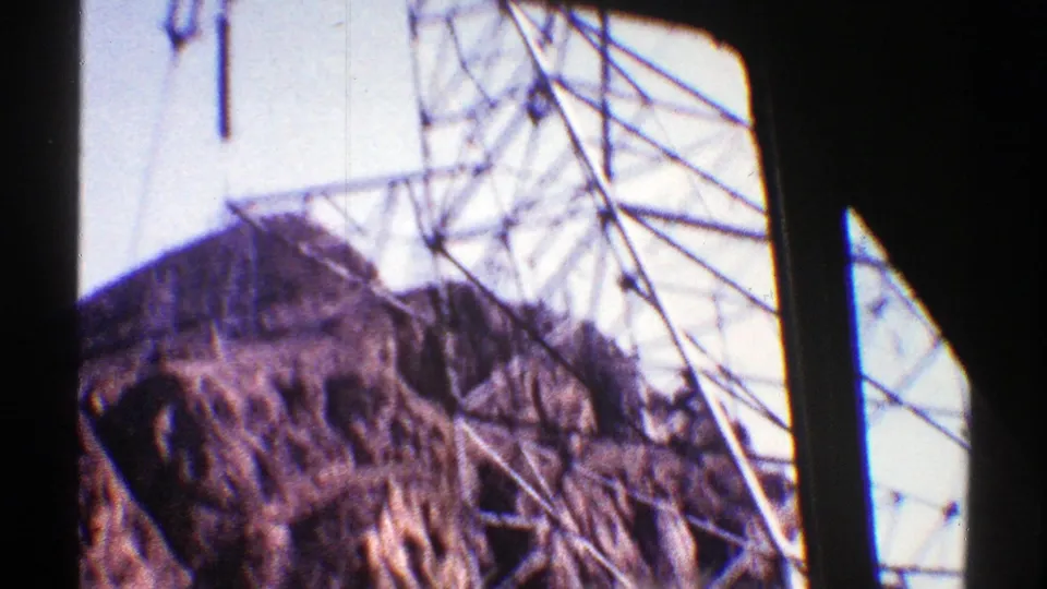 Grey steel transmission tower rises across the frame over rugged Arizona desert terrain in grainy 8mm footage.