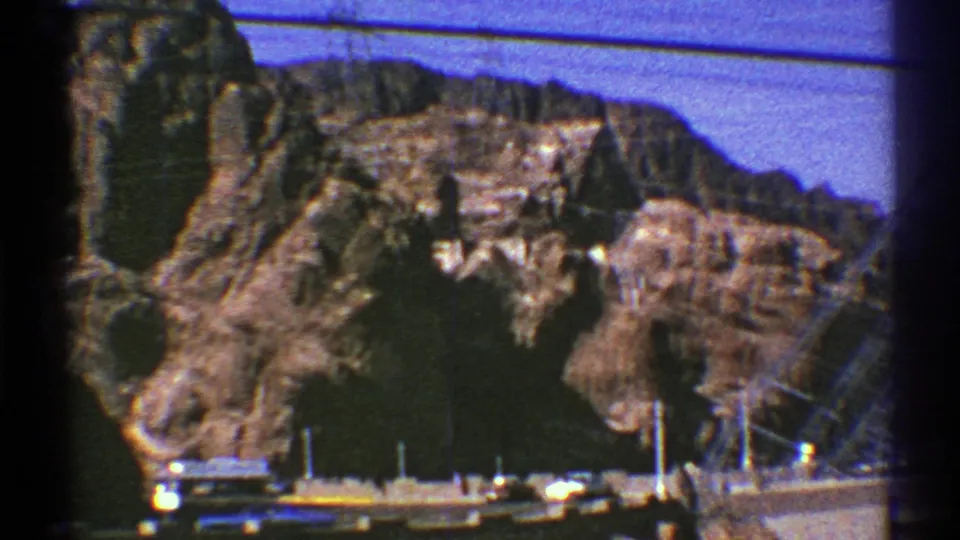 Roadside 8mm view of rocky Southwest terrain, overhead wires, small vehicles, and utility infrastructure.