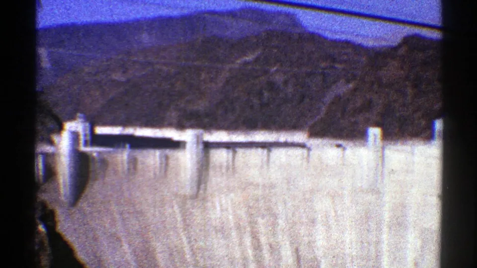 1969 Arizona 8mm frame focusing on a tall concrete dam face with brown desert mountains and dark film edge visible.