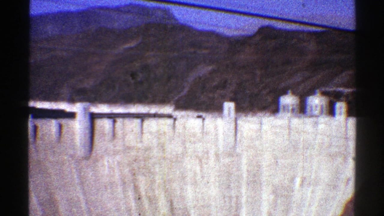 Concrete dam face below desert hills and blue sky.