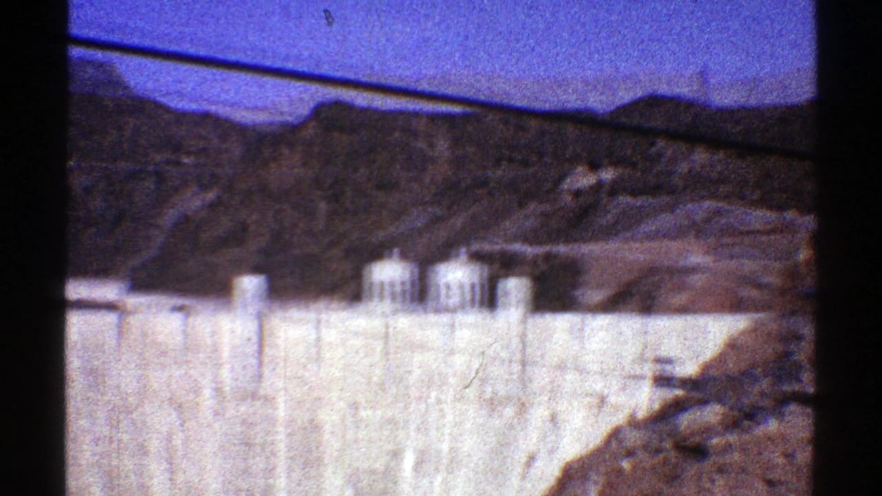 Hoover Dam appears across the frame with tower structures, canyon slopes, and dark gate shadows from the 8mm scan.