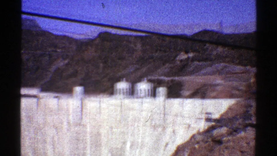 Hoover Dam appears across the frame with tower structures, canyon slopes, and dark gate shadows from the 8mm scan.