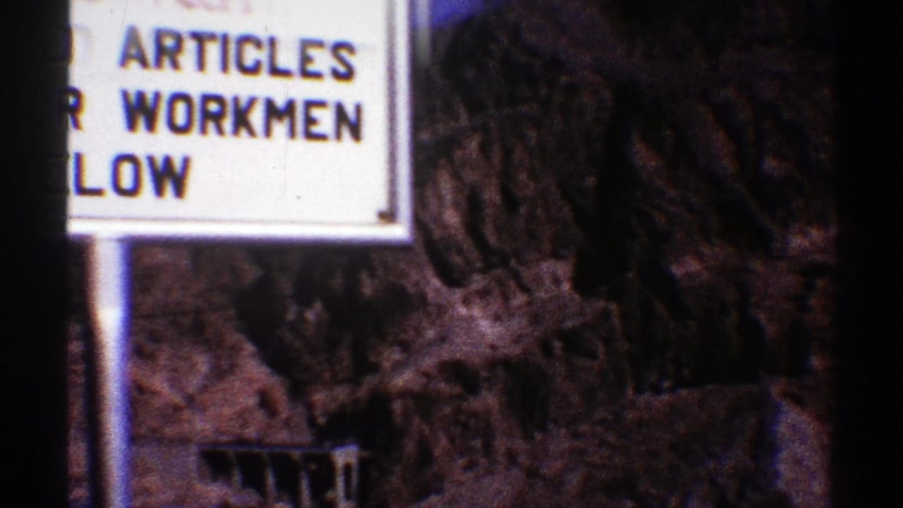 Warning sign with dam and rocky mountain terrain behind it.